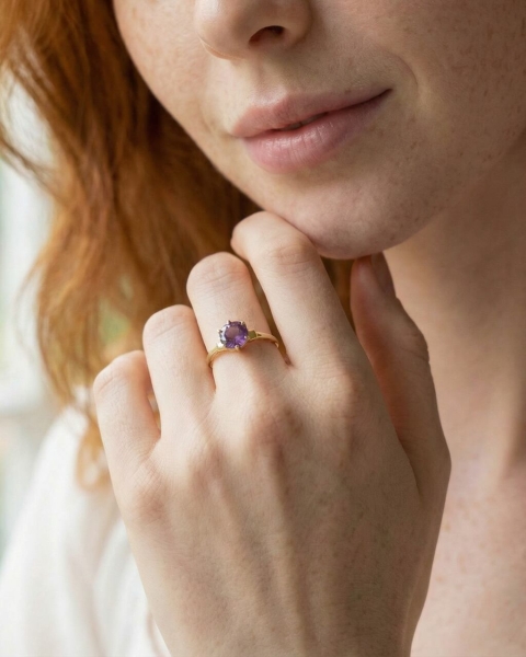 Zbliżenie na dłoń kobiety z pierścionkiem z ametystem w złoconej oprawie, delikatna biżuteria ByLucy noszona na co dzień.