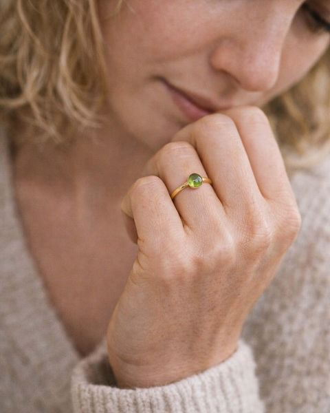 Zbliżenie na pierścionek z gładkim perydotem w złoconej oprawie na palcu kobiety, minimalistyczna biżuteria ByLucy.