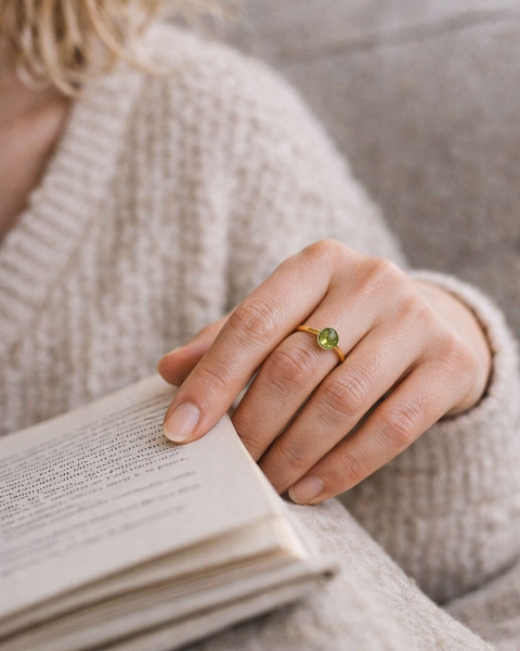 Dłoń kobiety noszącej delikatny złocony pierścionek z naturalnym perydotem, biżuteria autorska ByLucy w codziennym ujęciu.