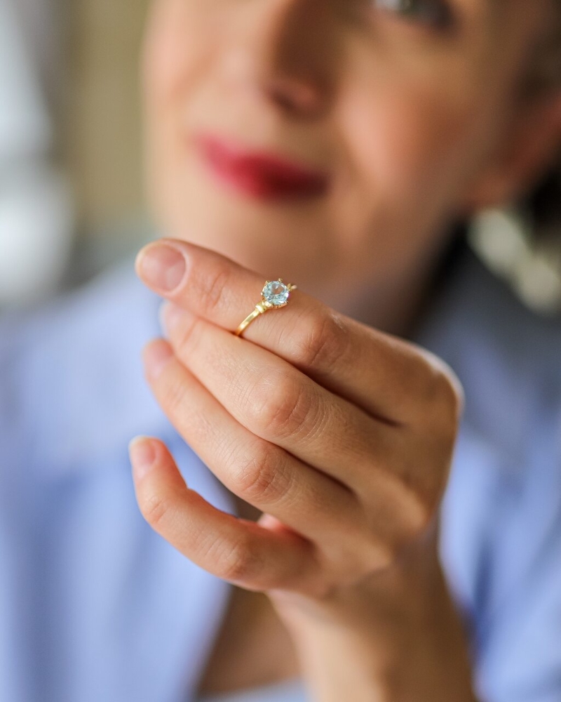 Zbliżenie na dłoń kobiety z pozłacanym pierścionkiem z niebieskim kamieniem po odświeżeniu biżuterii ByLucy.